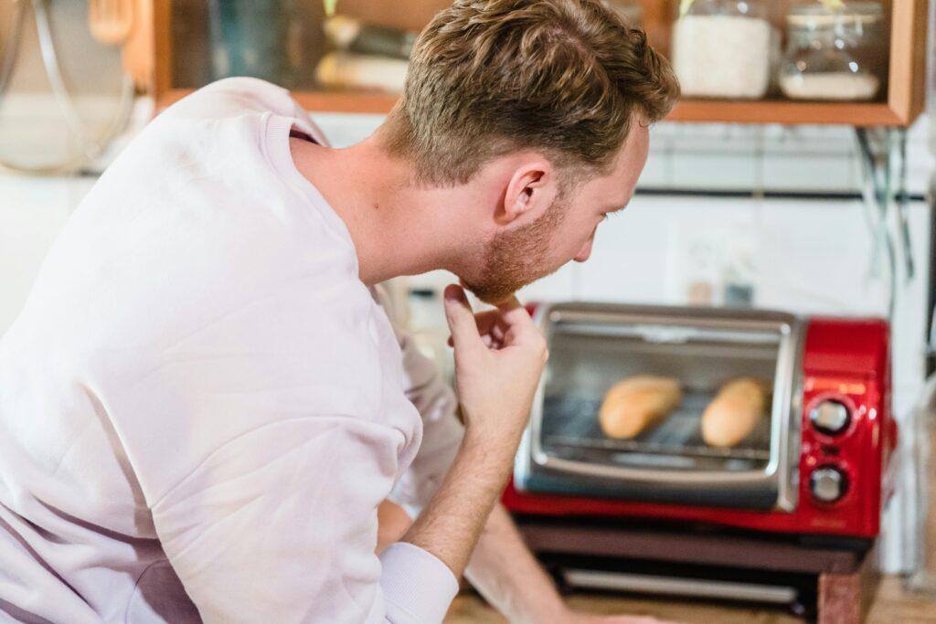 A man observes bread baking in a toaster oven in a cozy kitchen setting.
